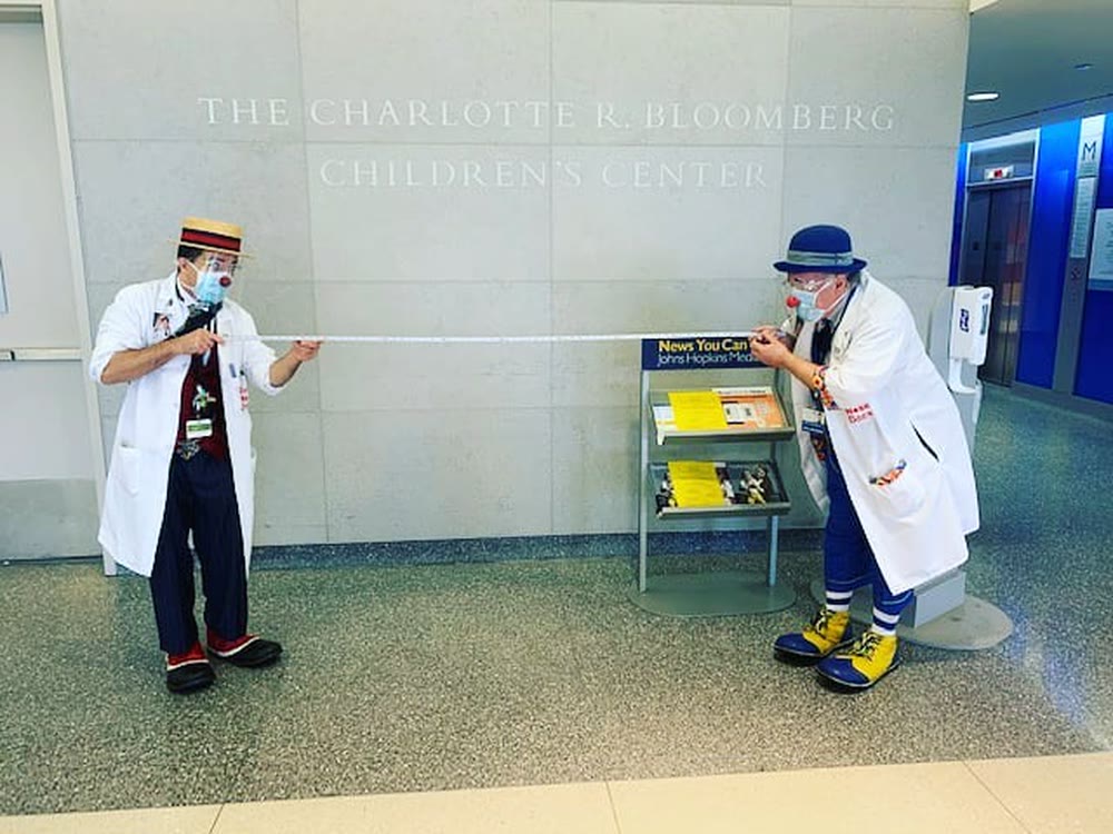 Two Red Nose Docs stretch a tape measure between them in the Charlotte R. Bloomberg Children&rsquo;s Center lobby.