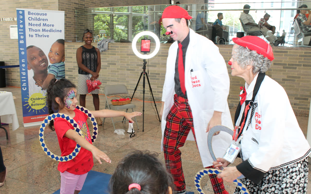 Two Red Nose Docs play a hoop game with children at a hospital community event.