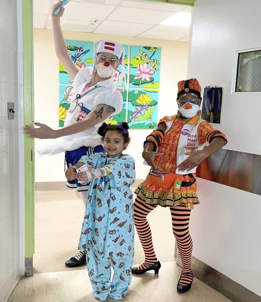 Two Red Nose Docs strike a pose in a doorway with a young patient between them.