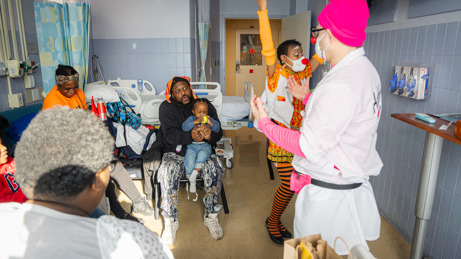 Two Red Nose Docs perform for a child and family on a hospital ward.